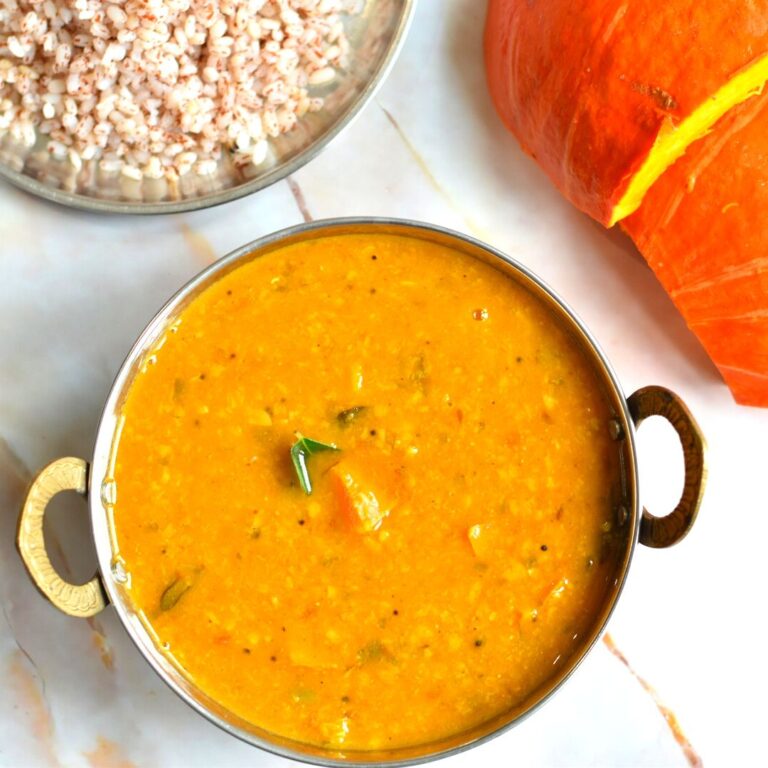 Instant Pot Pumpkin Sambar served in a small kadai/wok. Seen in the background is pumpkin and some red rice.