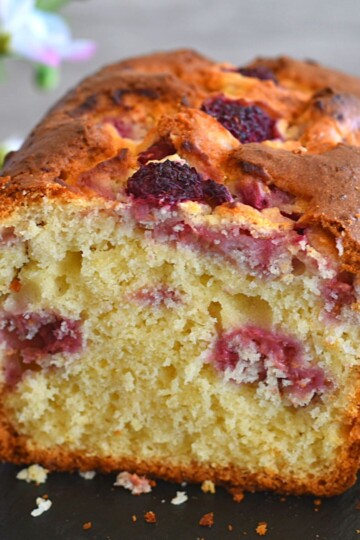 Front view of Gluten-Free Lemon Raspberry Coconut Cake on a black cheese board with some flowers in the background