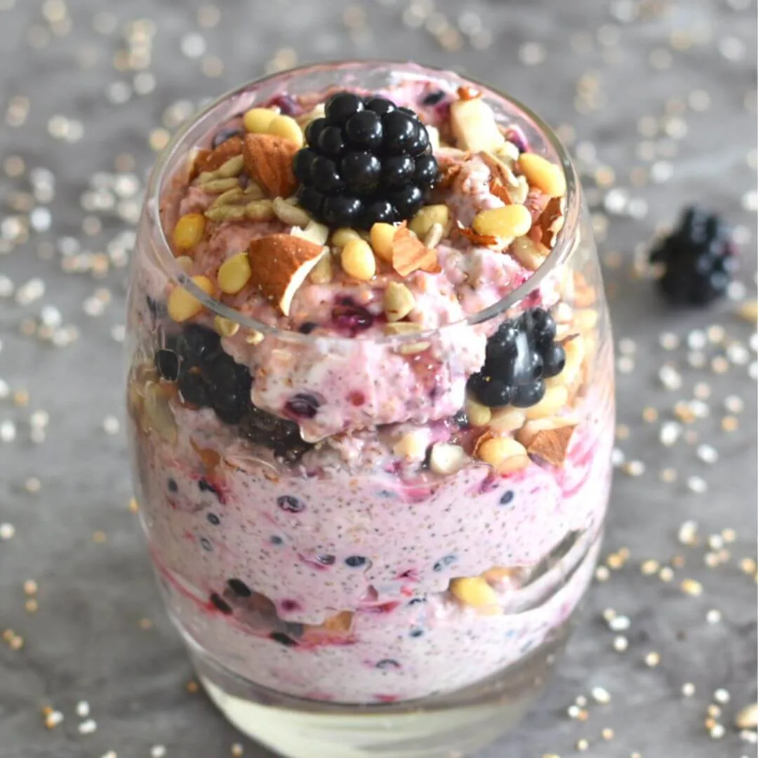 Amaranth Blackberry Yogurt Parfait served in a glass with some scattered amarnath or rajgira seen in background.