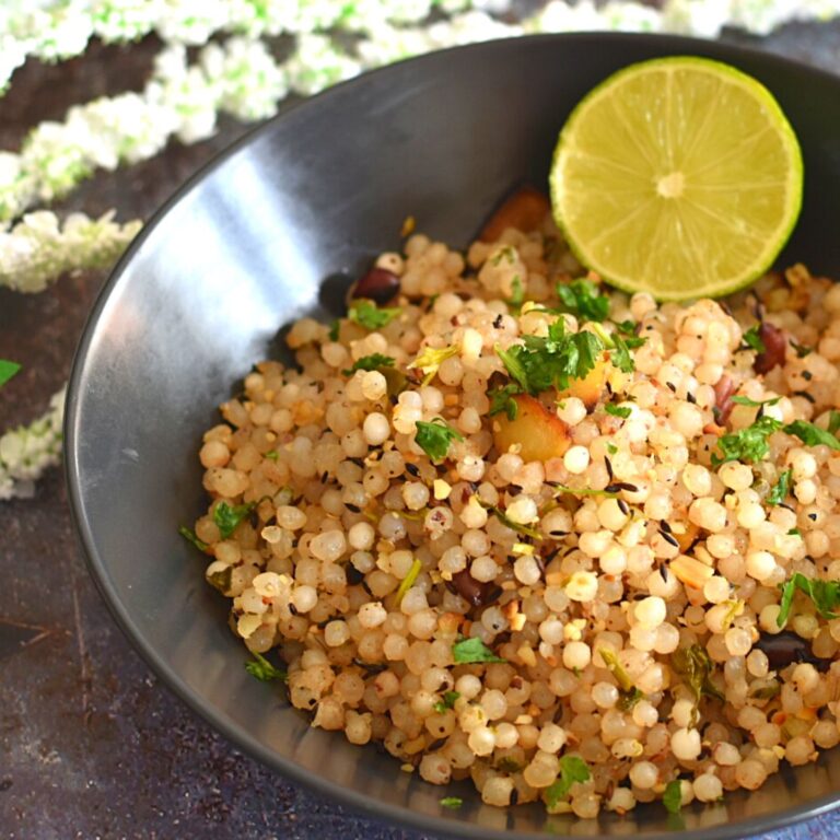 Sabudana Khichdi served in a black bowl with a garnish of lemon wedge and some flowers in the background