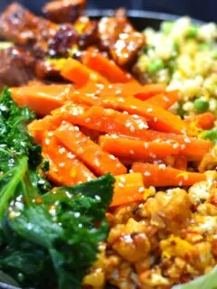 Vegan orange Sizzler with cauliflower, tofu, kale, carrots, peas and quinoa on a black cast iron plate.