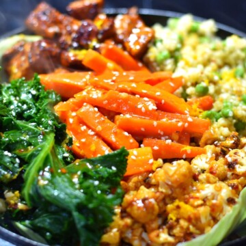 Vegan orange Sizzler with cauliflower, tofu, kale, carrots, peas and quinoa on a black cast iron plate.