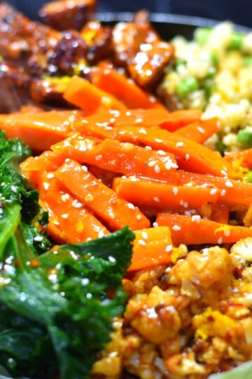 Vegan orange Sizzler with cauliflower, tofu, kale, carrots, peas and quinoa on a black cast iron plate.