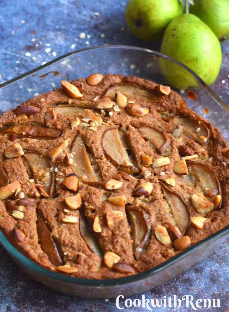 Oats Pear Apple Cake in a baking tray, with some pears in the background.
