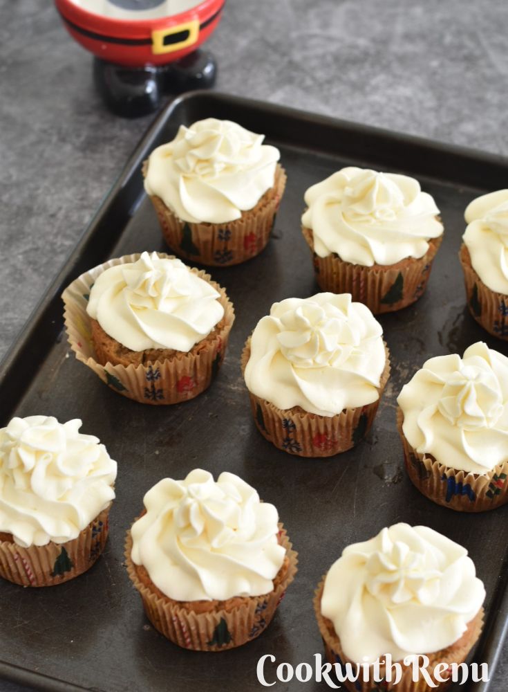 A tray of eggless and Vegan Vanilla Cupcakes on a grey board with Santa candle stand seen in the background.