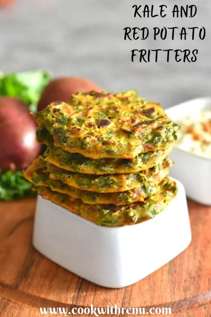 Stack Kale and Potato Fritters in a white upside-down bowl. In the background are some potatoes and kale along with a bowl of yogurt.