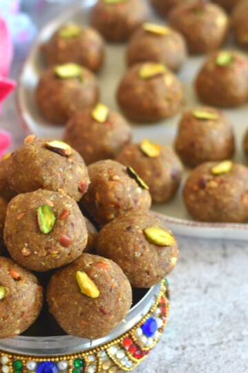 Methi and Gond Ladoo in a designer multi colour box with a few ladoos seen behind in a plate and some flower.