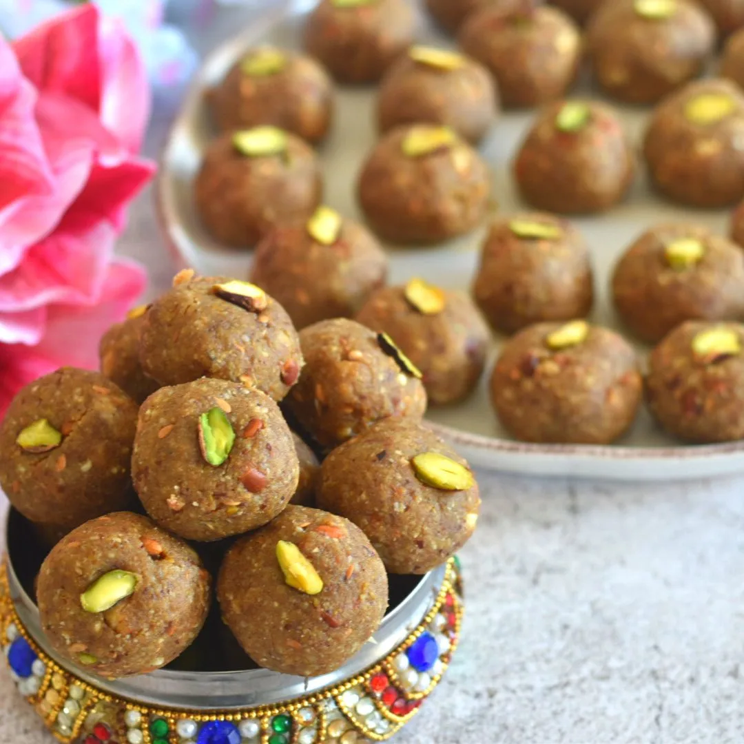 Methi and Gond Ladoo in a designer multi colour box with a few ladoos seen behind in a plate and some flower.