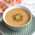 Low carb Cabbage Moong Sprout Soup in a green bowl with a garnish of moong sprout. Seen behind are some red and pink flowers.