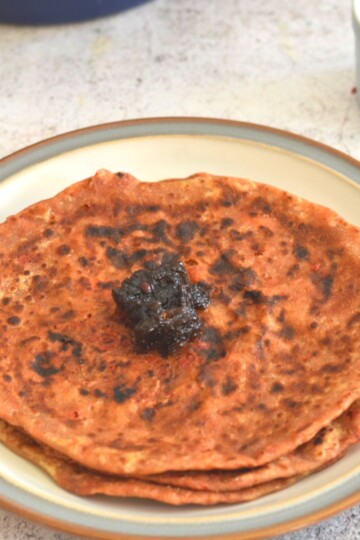 Leftover Veg and Paneer Paratha served in a plate with grey and brown lining. Lemon oil free pickle is served on top.