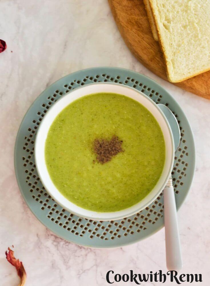 One-pot Celery and Broccoli Soup served in a green designer bowl with some bread slices in the background.