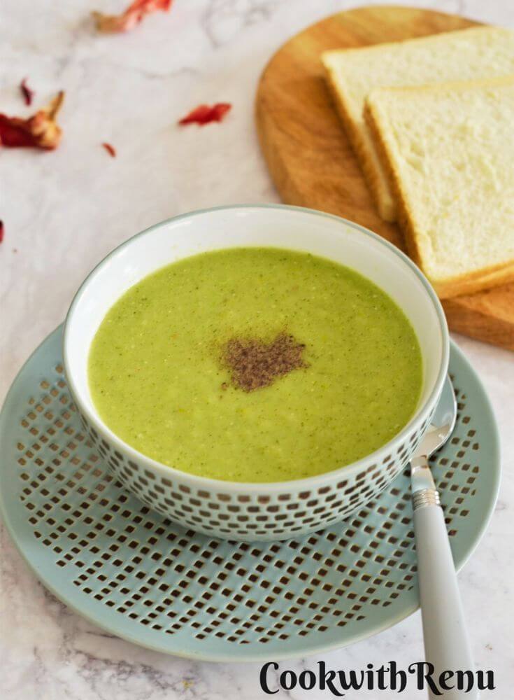 Healthy Celery and Broccoli Soup served in a green designer bowl with some bread slices in the background.