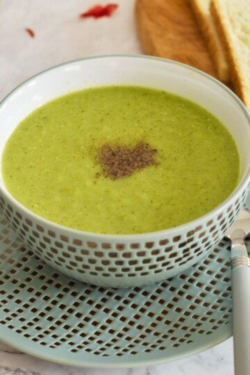 Healthy Celery and Broccoli Soup served in a green designer bowl with some bread slices in the background.