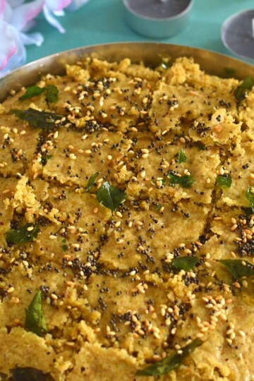 Gluten-free Millet Dhokla in a steel plate just after the tempering. Seen in the background are some flowers and candles.