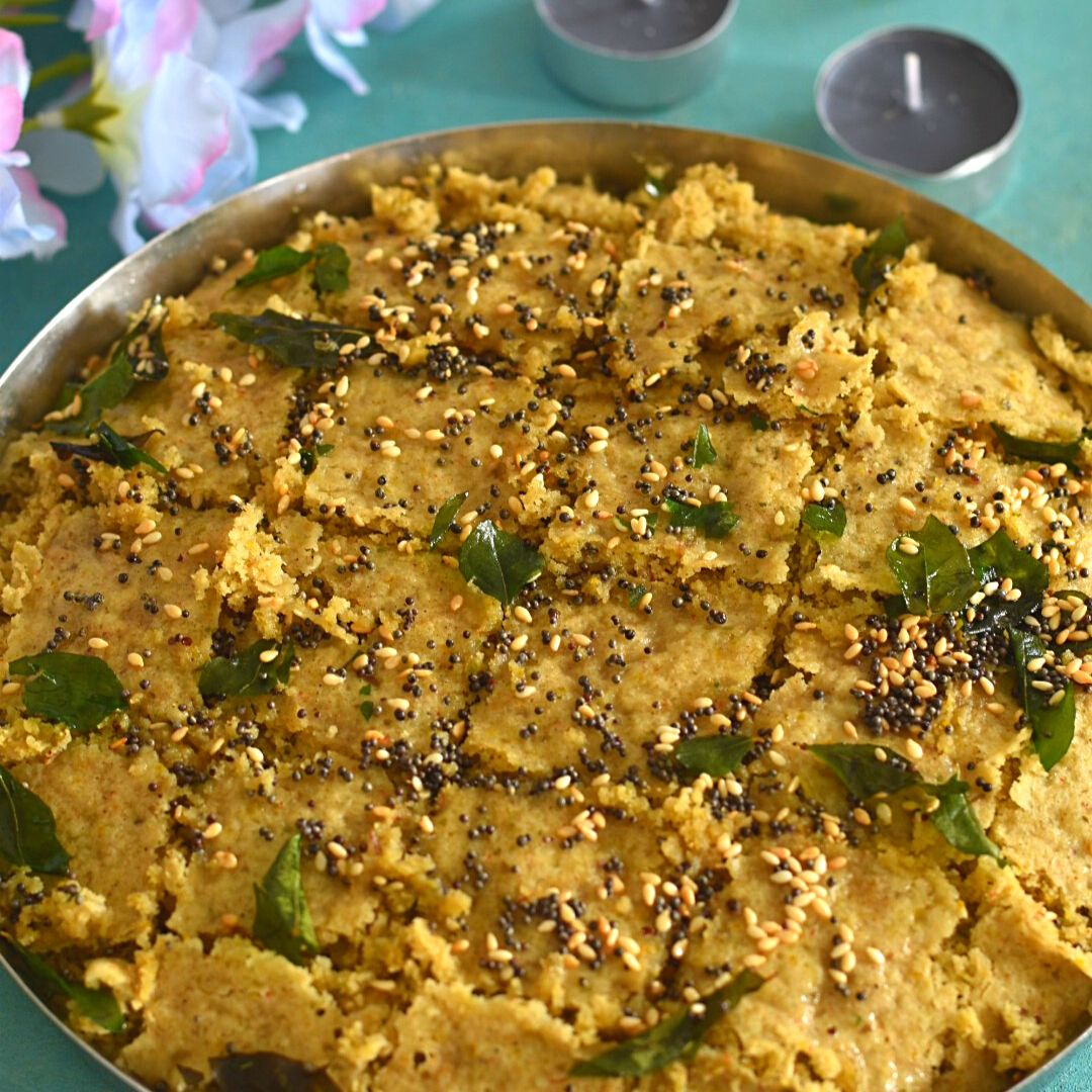 Gluten-free Millet Dhokla in a steel plate just after the tempering. Seen in the background are some flowers and candles.