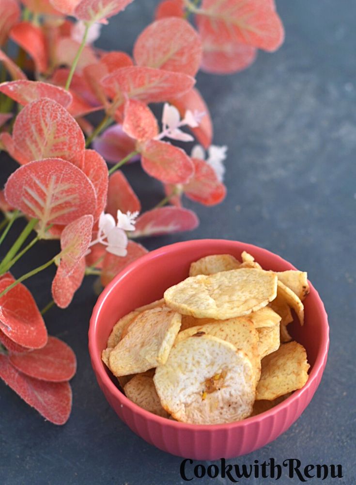 The top look of Arbi or Taro root Chips in a red bowl with some red flowers in the background.