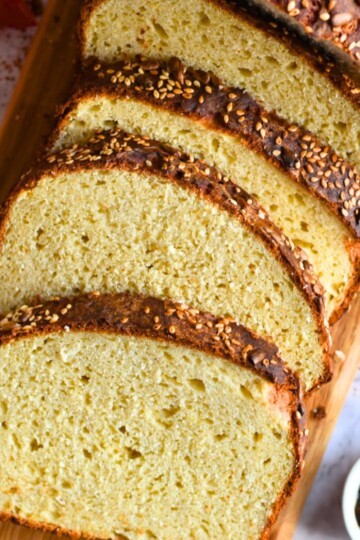 Slices of Gluten Free Sandwich Bread on a brown cheese board with some butter and jam on the side.