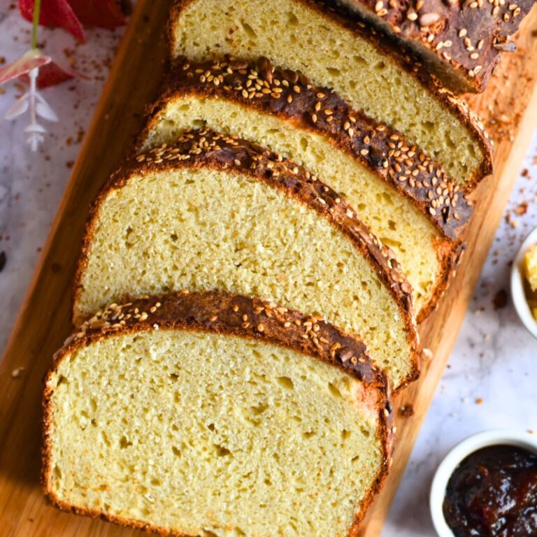 Slices of Gluten Free Sandwich Bread on a brown cheese board with some butter and jam on the side.