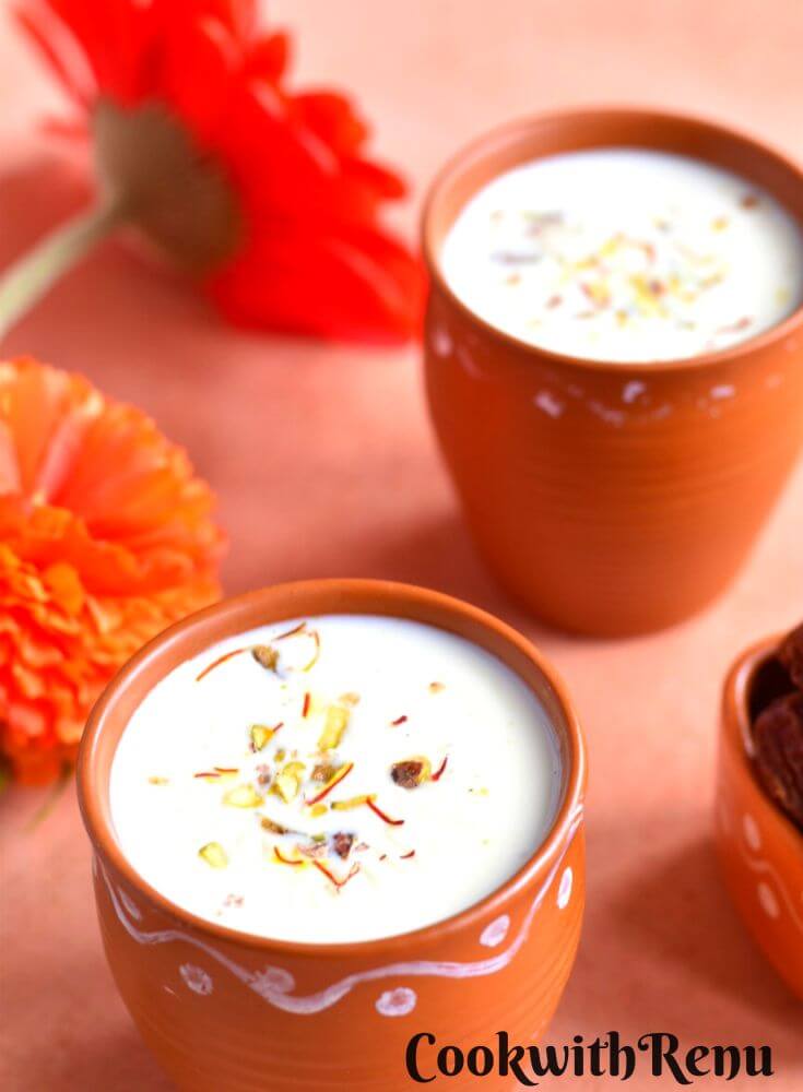 Khajoor Dudh served in 2 brown cups with some dates and flowers in the background