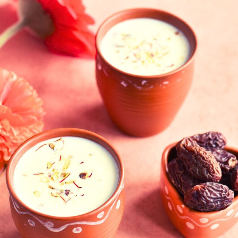 Khajoor Dudh served in 2 brown cups with some dates and flowers in the background