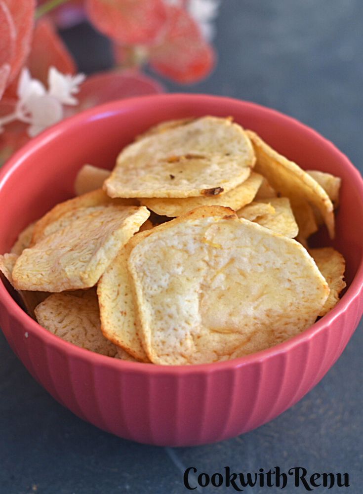 Close-up look of Arbi Chips in a red bowl with some red flowers in the background.