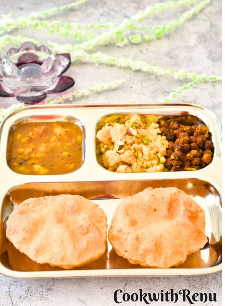 Navratri Ashtami /NavamiThali in a steel plate, with puri, halwa, channa, and aloo sabji. Seen in the background is rose candle holder and some flowers.