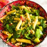 Vegan Summer Pasta Salad in a colorful red bowl. Some artificial flowers in the background