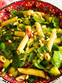 Vegan Summer Pasta Salad in a colorful red bowl. Some artificial flowers in the background
