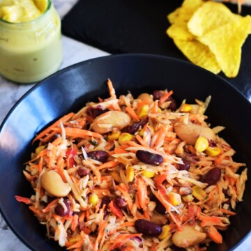 Easy Vegan Coleslaw with beans served in a black bowl with some chips and mayo in a bottle on the side.
