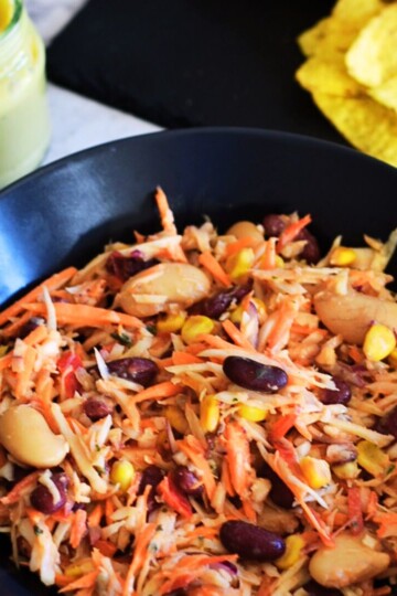 Easy Vegan Coleslaw with beans served in a black bowl with some chips and mayo in a bottle on the side.