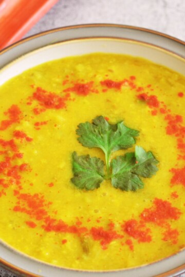 Savory Rhubarb Dal with a garnish of coriander and red chili powder served in a white bowl with grey lining and seen in the background is rhubarb