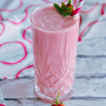 Sugar Free Strawberry Milkshake served in a glass with a garnish of strawberry and a straw in the glass. seen in the front are 2 strawberries.