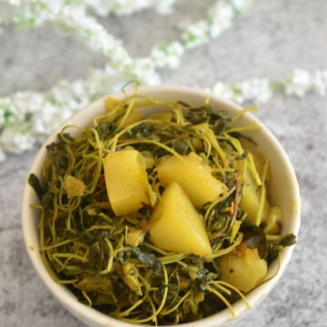 Aloo Methi Bhaji served in a white bowl with some artificial flower behind.