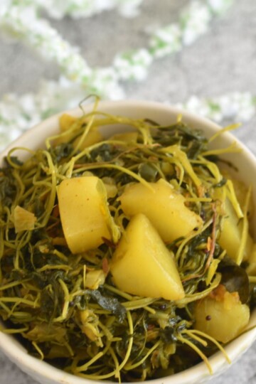 Aloo Methi Bhaji served in a white bowl with some artificial flower behind.