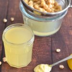 Aquafaba in a jar and seen in the background are some chickpeas and a spoon of vegan mayo in the front.
