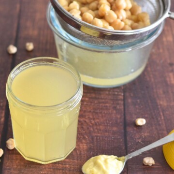 Aquafaba in a jar and seen in the background are some chickpeas and a spoon of vegan mayo in the front.