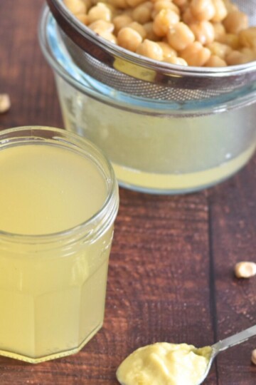 Aquafaba in a jar and seen in the background are some chickpeas and a spoon of vegan mayo in the front.