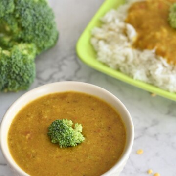 Instant Pot Broccoli Dal served in a white bowl, with some rice and dal served on a green plate in the background and some broccoli in the background.