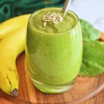 Avocado Banana Spinach Smoothie served in a glass bowl with some sunflower seeds as garnish and seen in background is banana and spinach.