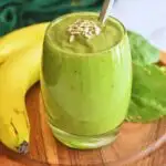 Avocado Banana Spinach Smoothie served in a glass bowl with some sunflower seeds as garnish and seen in background is banana and spinach.