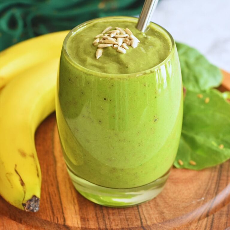 Avocado Banana Spinach Smoothie served in a glass bowl with some sunflower seeds as garnish and seen in background is banana and spinach.