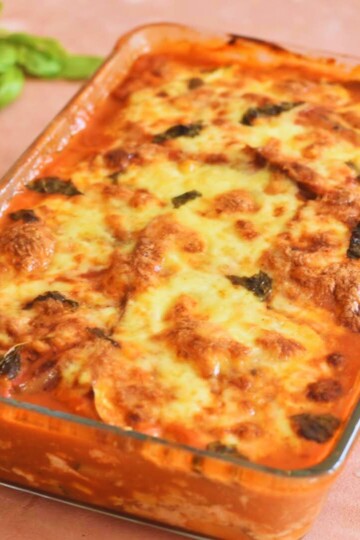 Zucchini and Aubergine Lasagna in a baking tray with few basil leaves on the side.