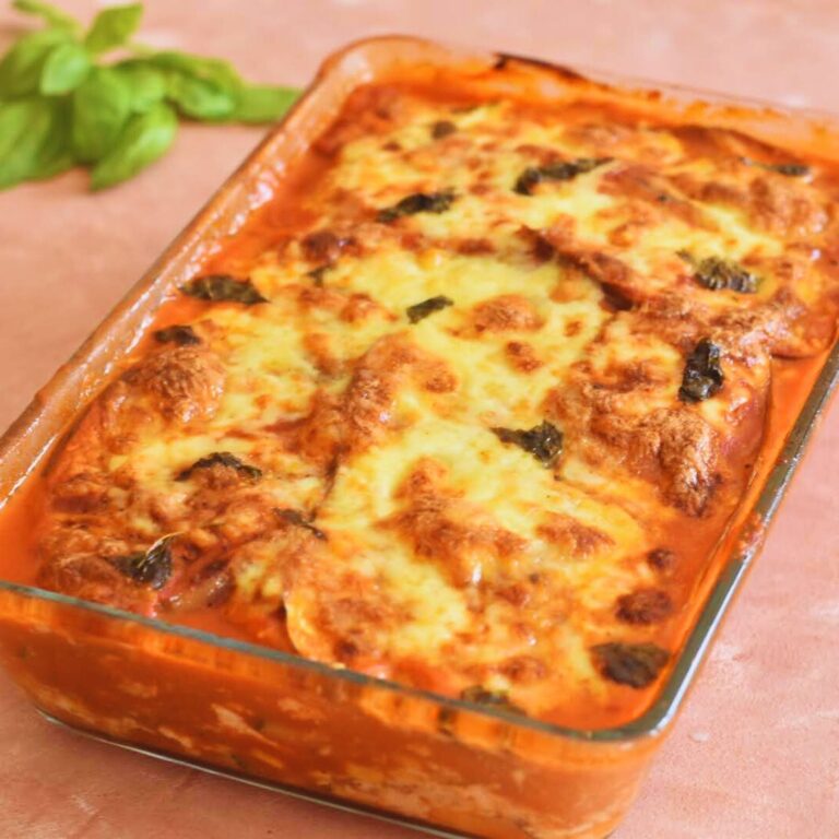 Zucchini and Aubergine Lasagna in a baking tray with few basil leaves on the side.