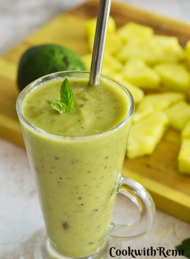 Pineapple Avocado Mint Smoothie served in 2 glasses with some pineapple slices and avocado in the background.