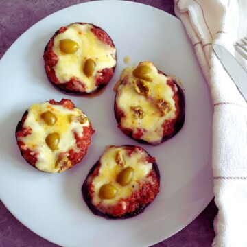 4 round slices of Eggplant Pizza served on a white plate.