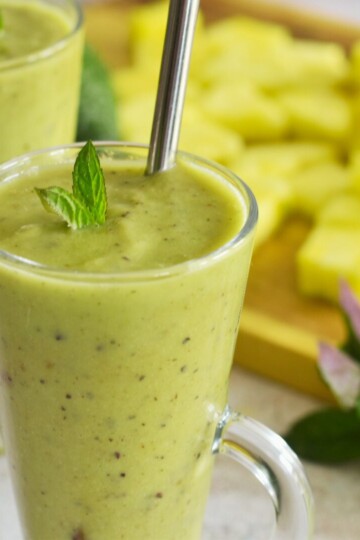 Pineapple Avocado Mint Smoothie served in 2 glasses with some pineapple slices and mint in the background.