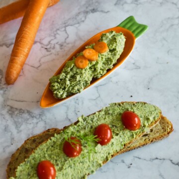 Carrot Greens Tofu Dip in an orange carrot shape plate. Seen in the background is a bread with tofu spread on it and few carrot and bread slices in basket.