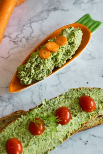 Carrot Greens Tofu Dip in an orange carrot shape plate. Seen in the background is a bread with tofu spread on it and few carrot and bread slices in basket.