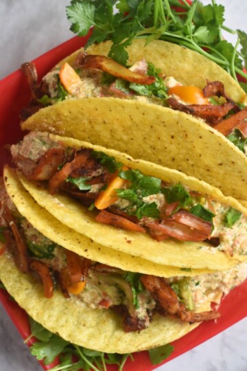 Three, easy Spicy Jackfruit Tacos served in a red plate with some cilantro served along.