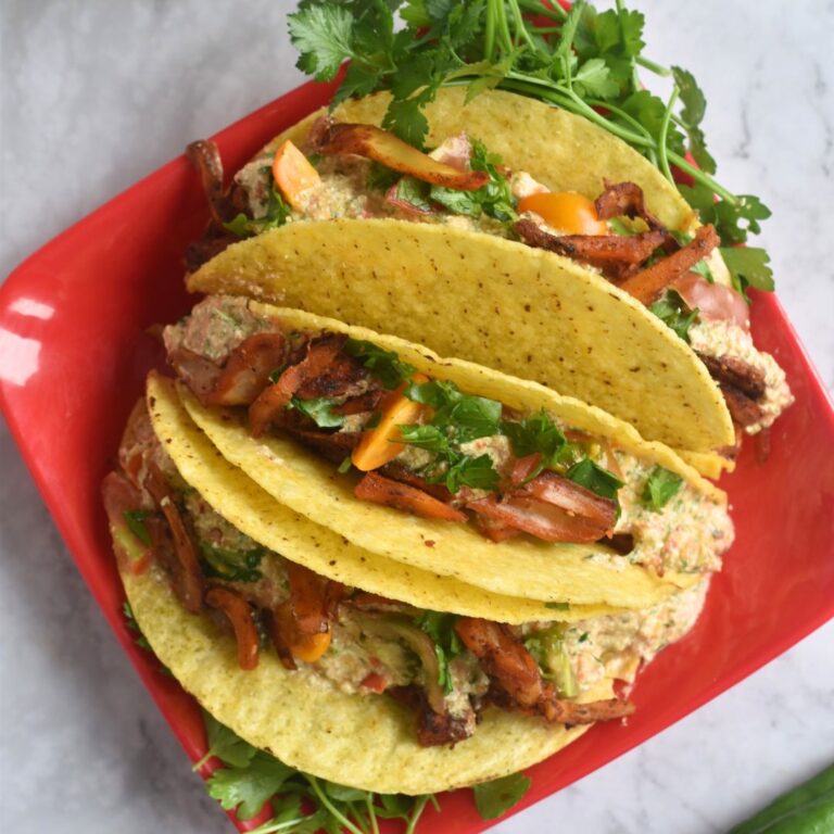 Three, easy Spicy Jackfruit Tacos served in a red plate with some cilantro served along.
